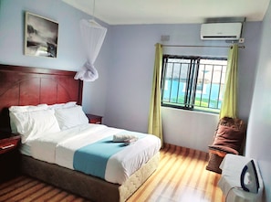 Een hotelkamer met een bed, een raam met gordijnen, een airconditioning en een schilderij aan de muur.