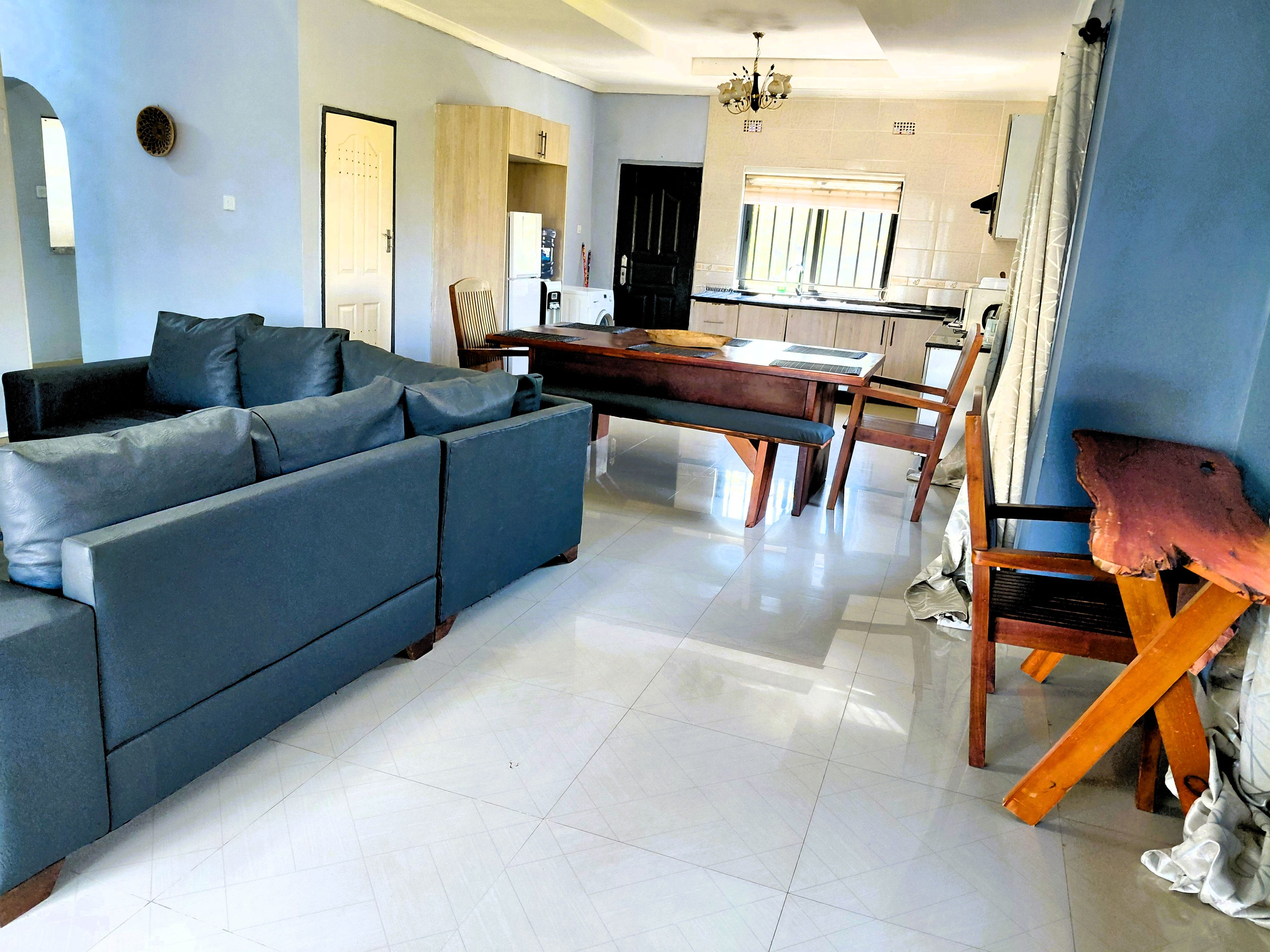 A modern living room with a sectional sofa, a dining table with chairs, and a kitchen area in the background.