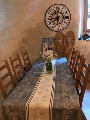 A dining table with a floral tablecloth, wooden chairs, a wall clock, and a poster on the wall.
