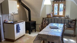Una cocina acogedora con estufa integrada, una mesa de comedor con mantel estampado y una ventana decorada con objetos.