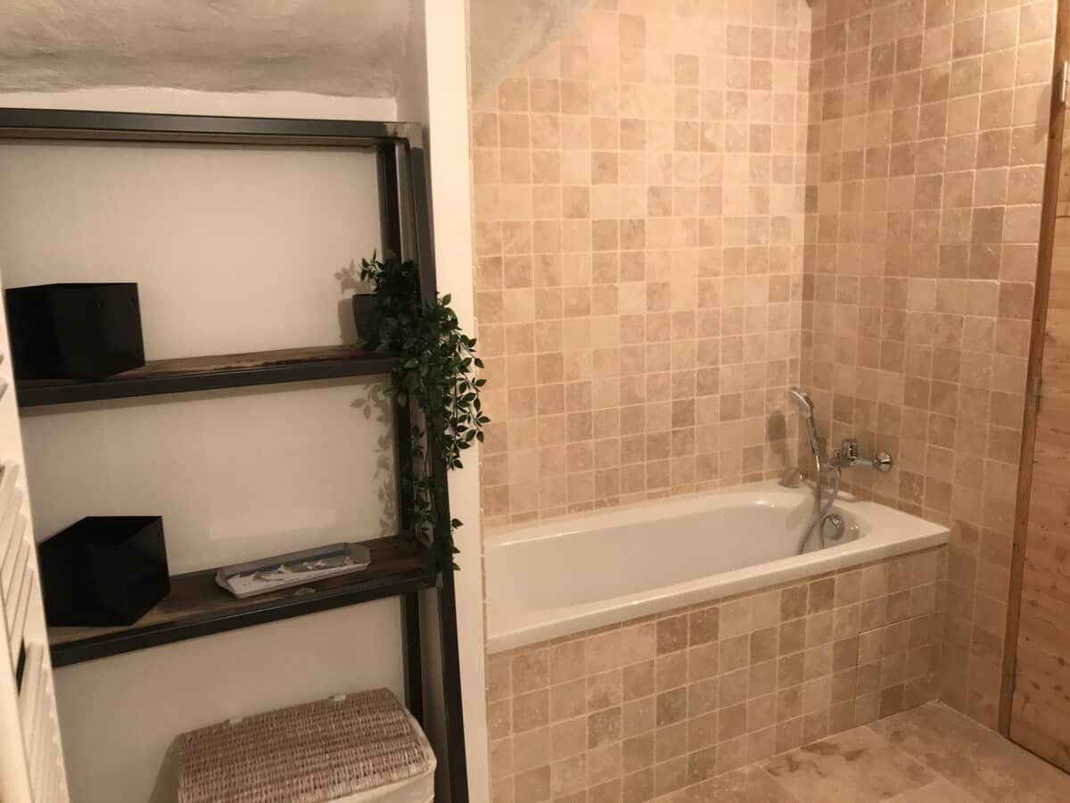 A bathroom with a bathtub, shelves, and a shower area.