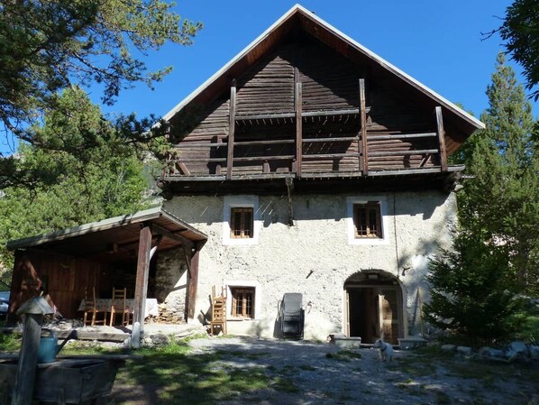 A rustic wooden house with a stone foundation, a wooden porch, and a small shed.