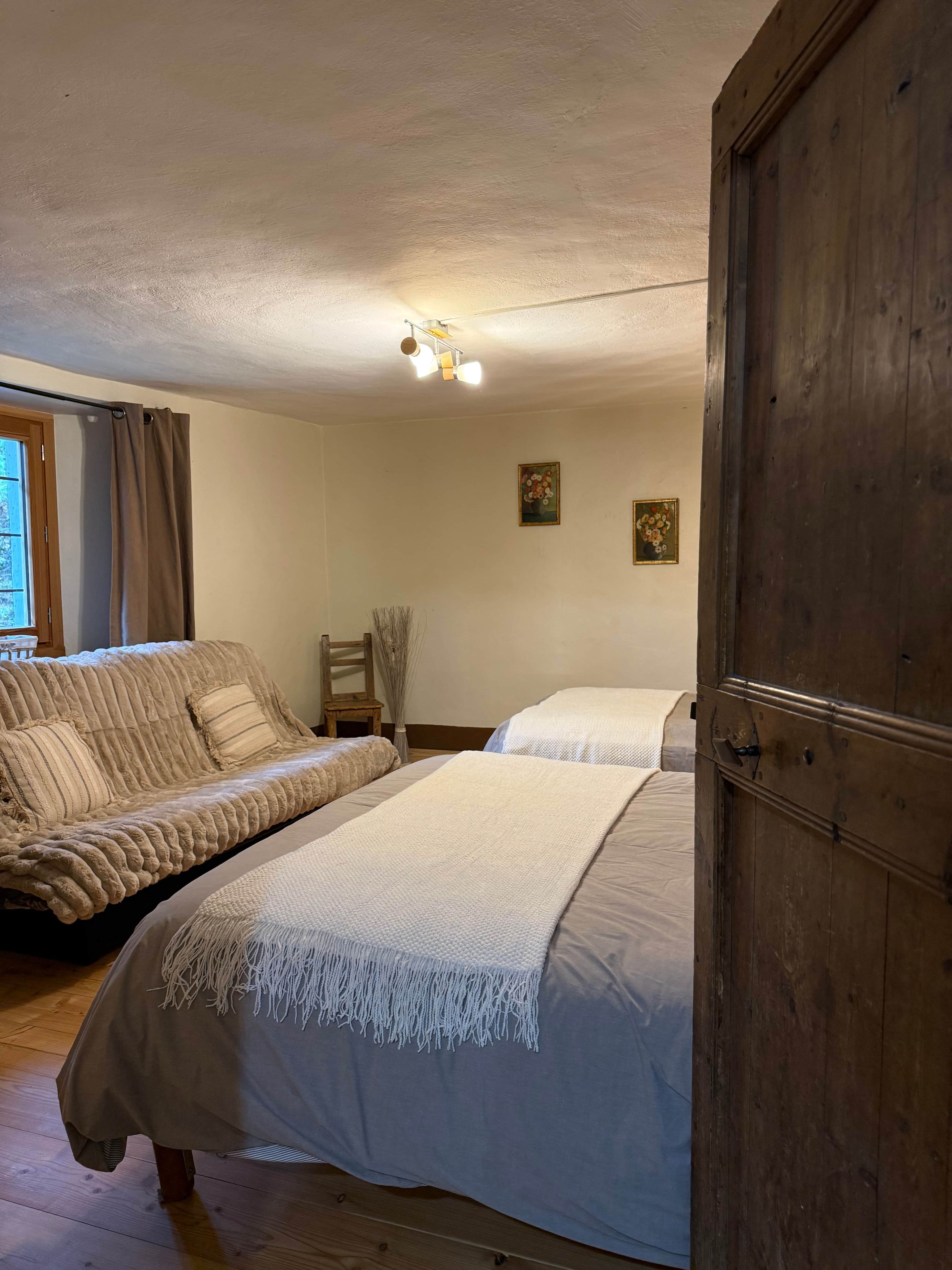 Une chambre à coucher avec un lit, un canapé, une armoire en bois et une fenêtre avec des rideaux.