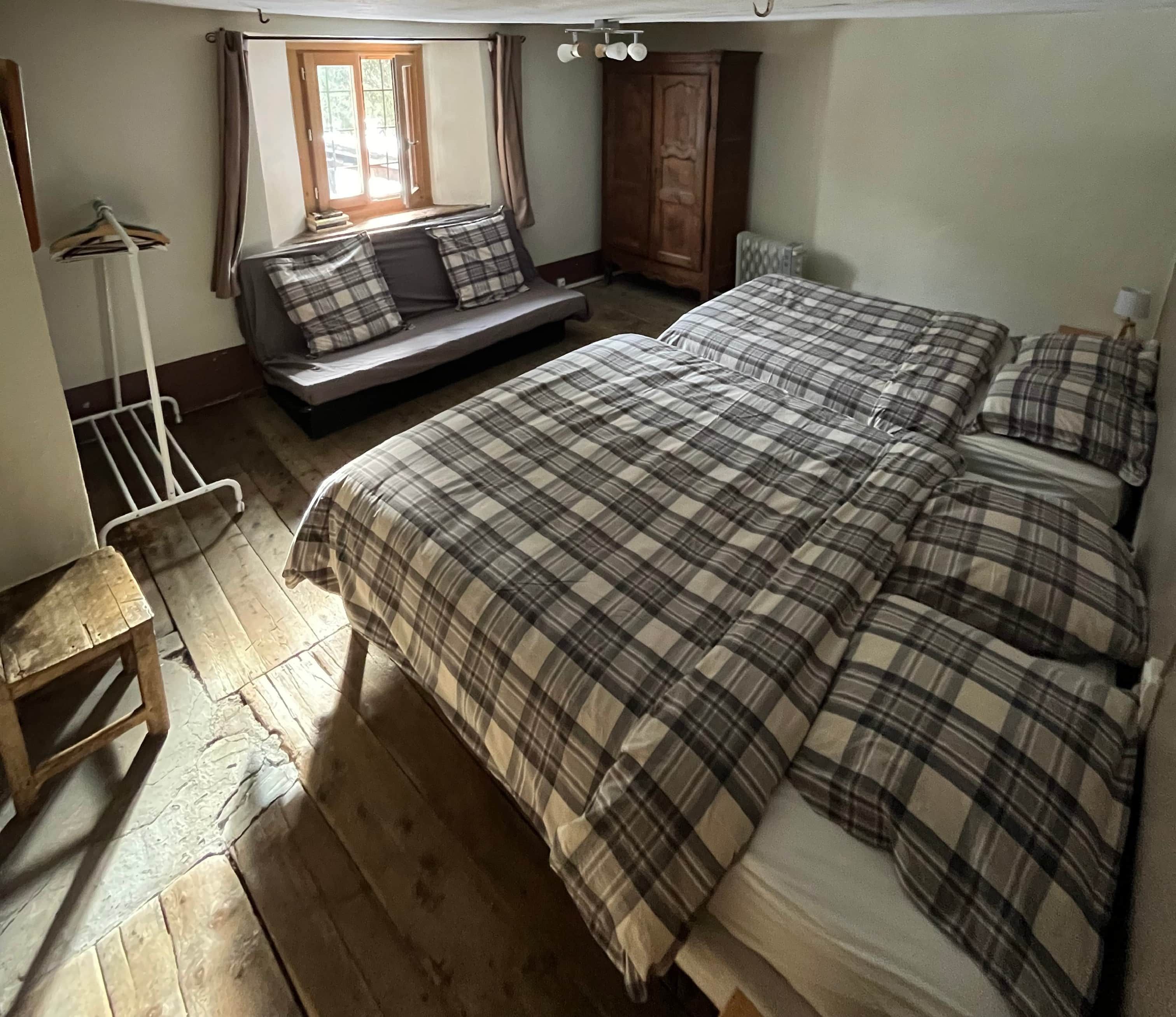 Une chambre à coucher avec un lit, un banc, une armoire et une fenêtre.