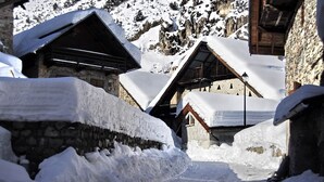 Un sendero estrecho cubierto de nieve, flanqueado por edificios de piedra con techos y balcones de madera.
