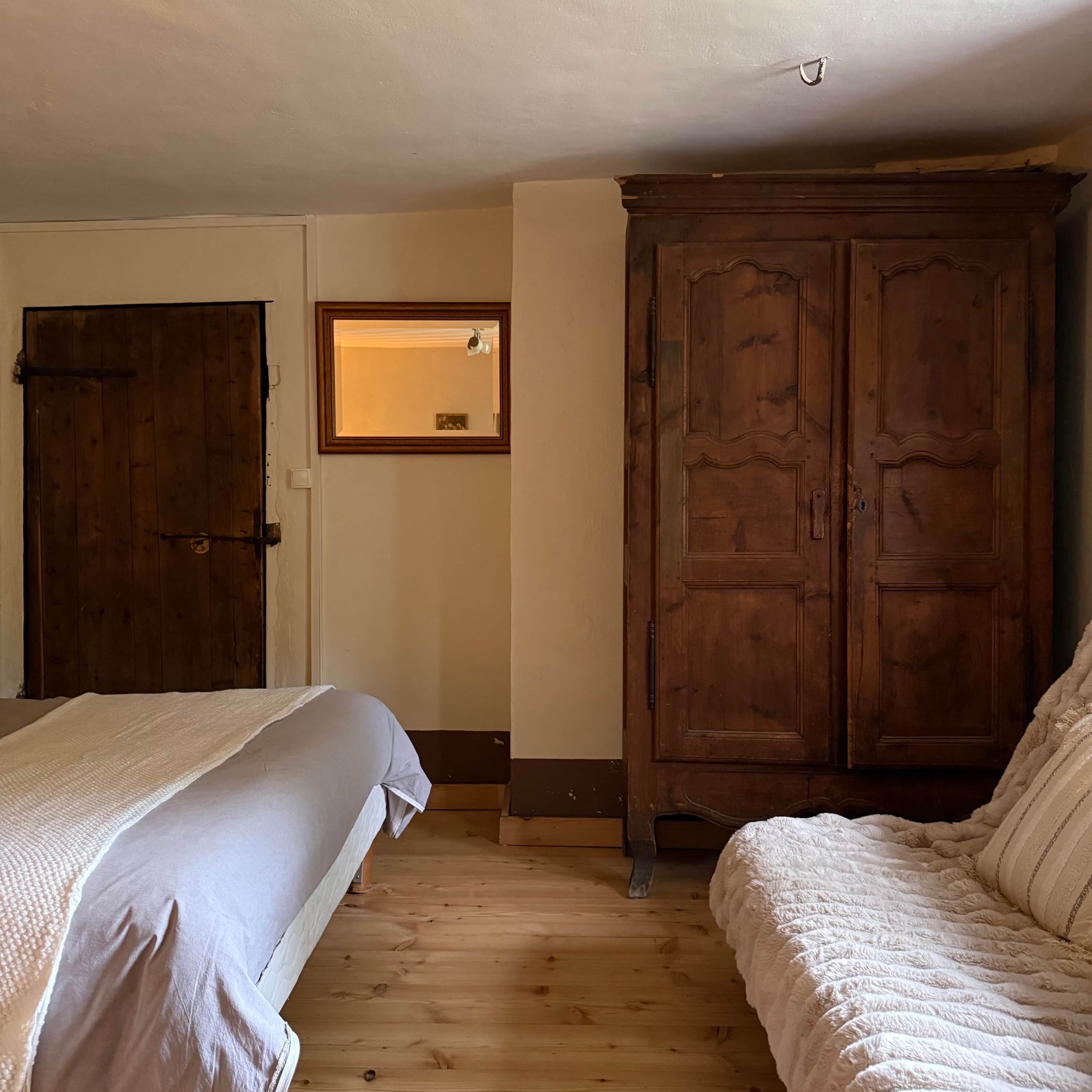 A bedroom with a wooden wardrobe, a bed with a white duvet, and a wooden floor.