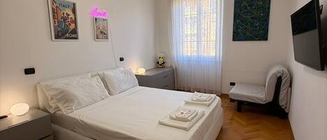 A bedroom with a bed, bedside tables, a chair, a television, and artwork on the walls.