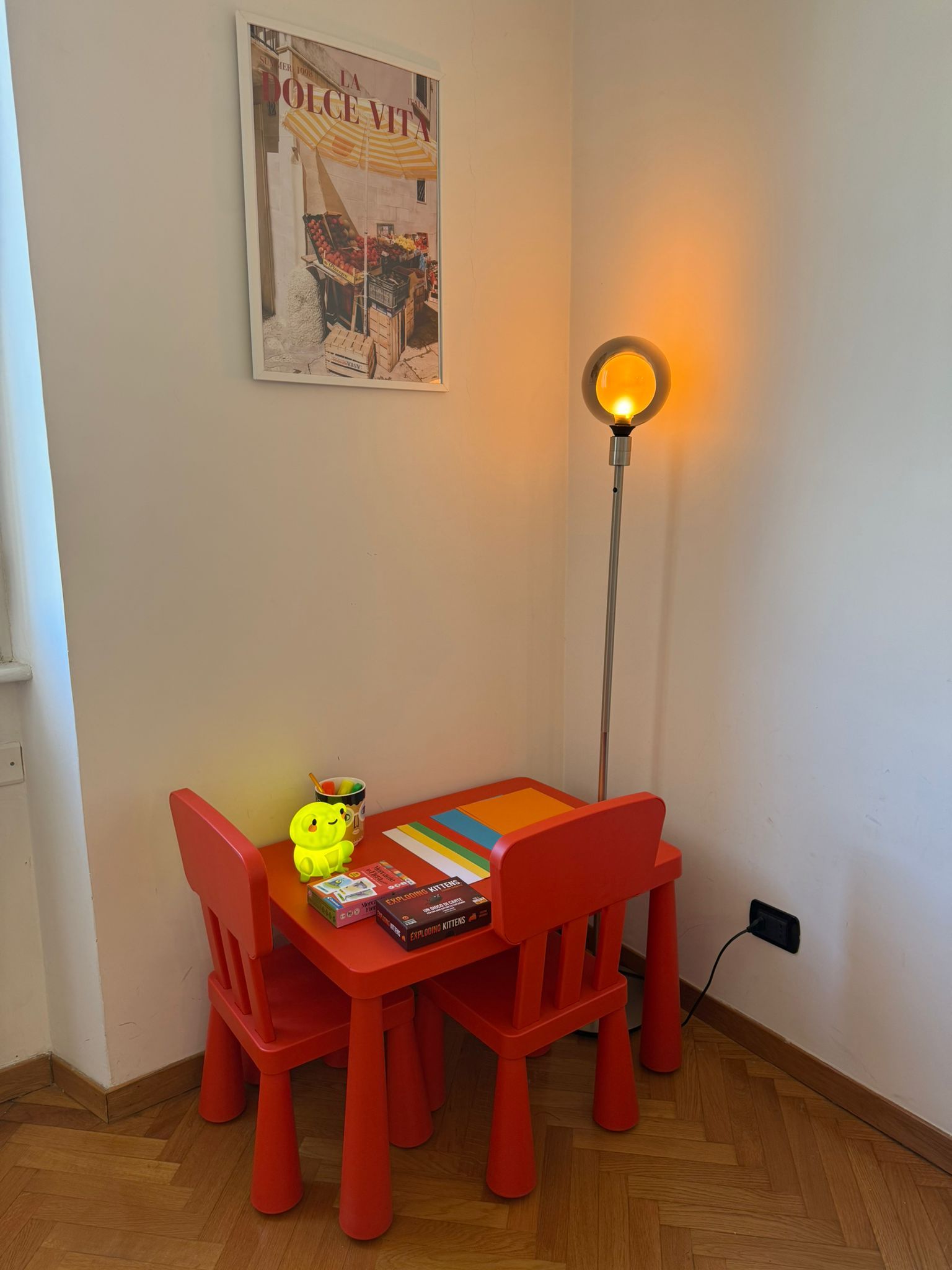 A corner room with a table, chairs, a floor lamp, and a poster on the wall.