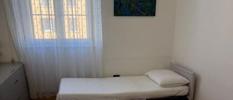 Habitación de hotel con dos camas, una ventana con cortinas traslúcidas, un cuadro en la pared y piso de madera.