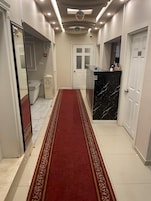 Corredor de hotel com carpete vermelho, balcão de recepção de mármore e porta branca com o número 104.