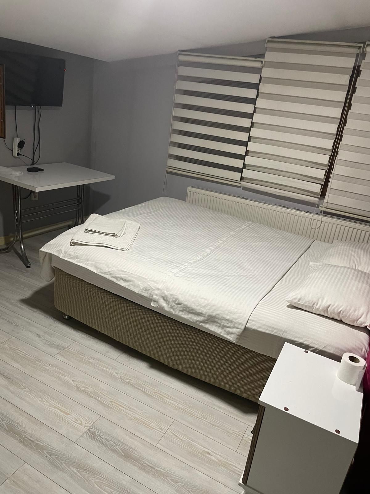 Quarto com cama, mesa de cabeceira com rolo de papel higiênico, radiador e televisão fixada na parede.
