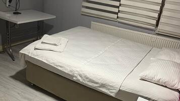Quarto com cama, mesa de cabeceira com rolo de papel higiênico, radiador e televisão fixada na parede.