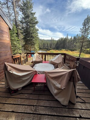 Un espace extérieur abrité, avec une table et des chaises, offrant une vue sur une zone boisée et un plan d’eau.