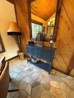 A room with a stone-tiled floor, a wooden ceiling, a blue cabinet with decorative items, and a lamp. - Charming 3-bedroom cabin in delightful Soda Springs getaway. Sorry no pets. (Soda Springs)