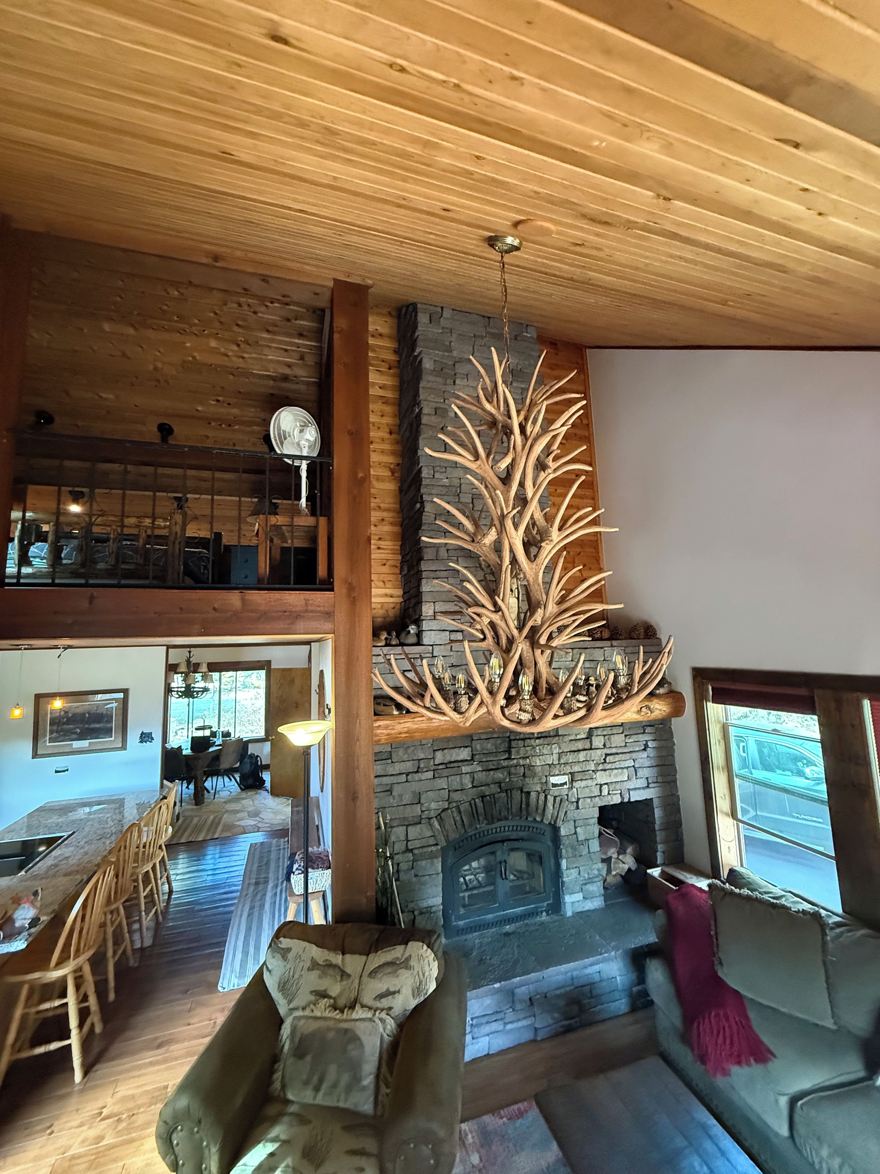 A spacious living area with a stone fireplace, a wooden ceiling, and a dining area with a view.