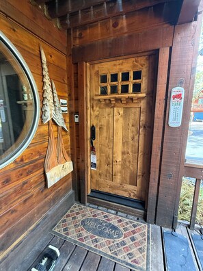 Une entrée de chalet en bois avec un paillasson, une porte en bois dotée d’une fenêtre et un panneau indiquant l’usage du matériel agricole.