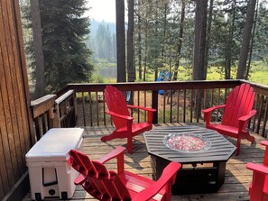 A wooden deck with a table and four red chairs, overlooking a forested area. - Charming 3-bedroom cabin in delightful Soda Springs getaway. Sorry no pets. (Soda Springs)