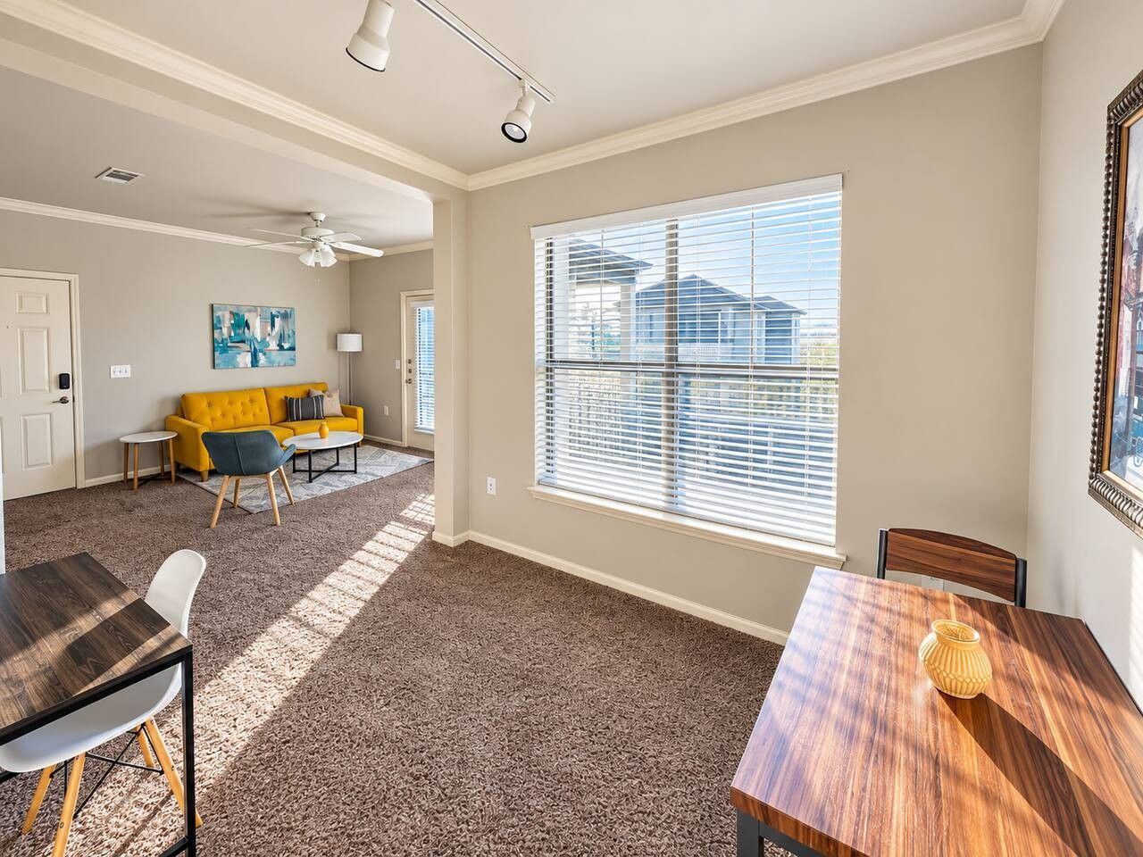 A spacious living area with a large window, a dining table, and a yellow sofa.