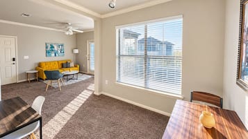 A spacious living area with a large window, a dining table, and a yellow sofa.