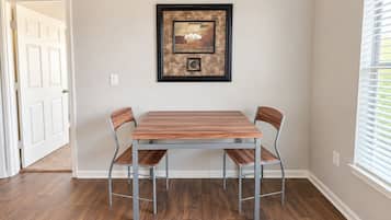 A dining area with a table and chairs, a framed artwork on the wall, and a window with blinds.