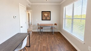 Una habitación con una mesa y sillas de comedor, un cuadro en la pared y una ventana con persianas.