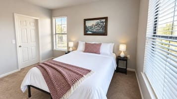 A bedroom with a bed, bedside lamps, a door, a window with blinds, and a painting on the wall.