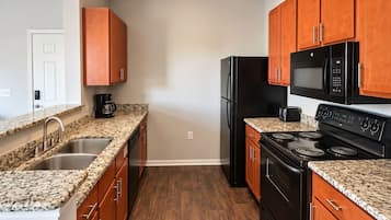A kitchen with granite countertops, a black refrigerator, a microwave, and a stove.