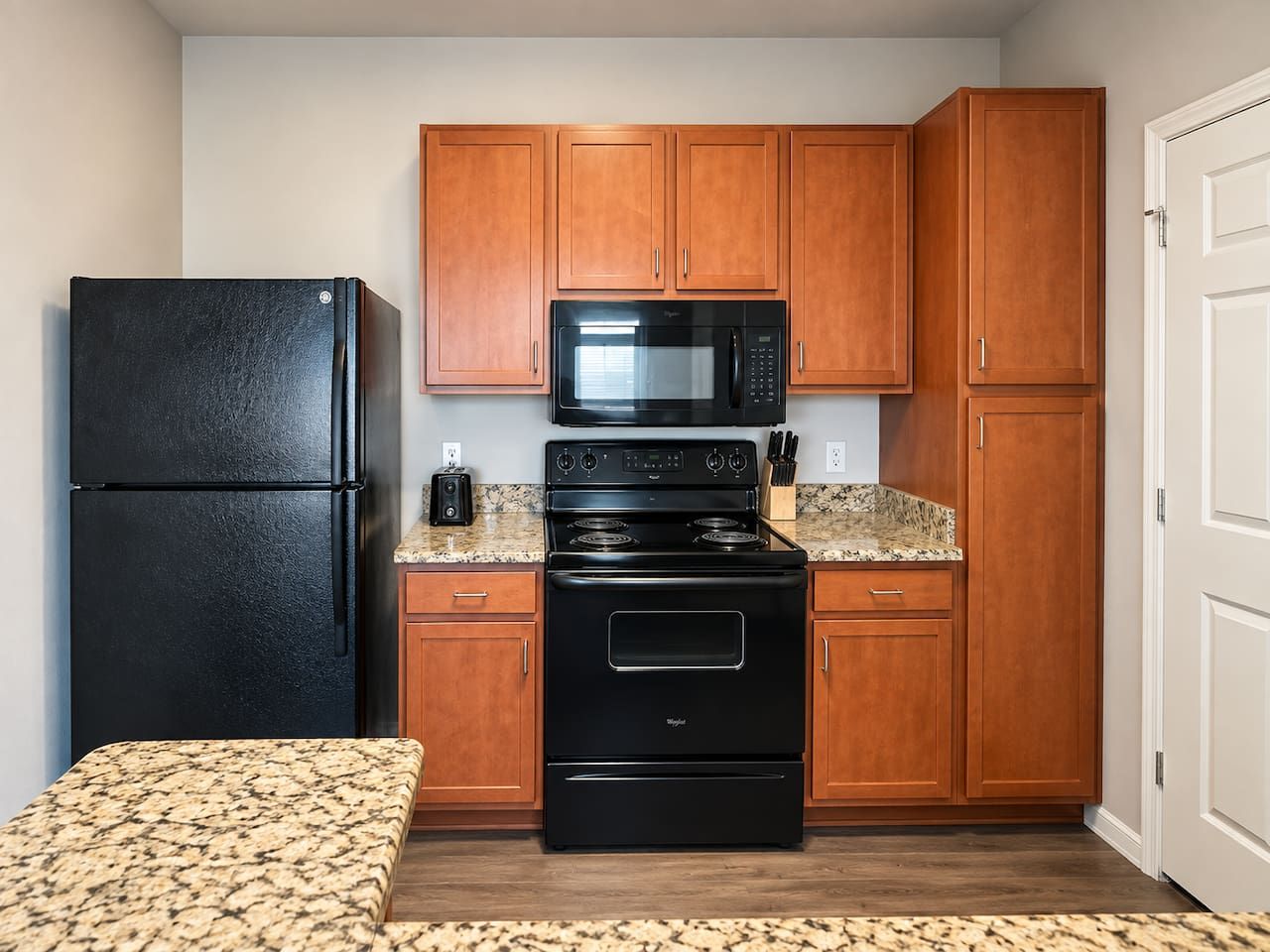 A compact kitchen with wooden cabinets, a black refrigerator, a microwave, and a stove.