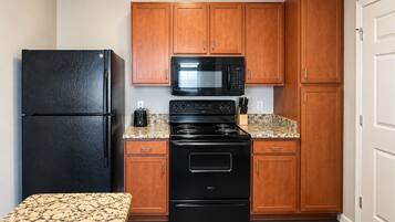 A compact kitchen with wooden cabinets, a black refrigerator, a microwave, and a stove.