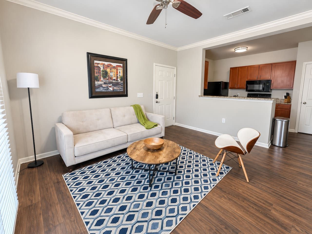A living room with a sofa, coffee table, and chairs, a patterned rug, and a kitchen in the background.