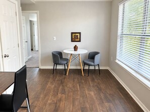 A room with a round table, two chairs, a door, a window with blinds, and a framed picture on the wall. - Sleepover | Radiant 1BD/1BA + Gym - Corpus Christi (Corpus Christi)