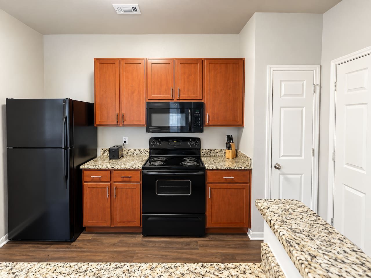 A compact kitchen with wooden cabinets, a black refrigerator, a microwave, and a stove.