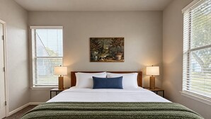 Ein ordentlich bezogenes Bett mit weißen Laken und einer grünen Decke, begleitet von zwei Nachttischlampen auf Holznachttischen.