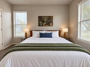 A neatly made bed with white linens and a green blanket, flanked by two bedside lamps on wooden nightstands. - Sleepover | Radiant 1BD/1BA + Gym - Corpus Christi (Corpus Christi)