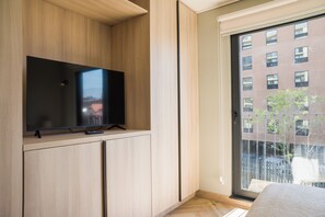 Ein modernes Zimmer mit einem Flachbildfernseher auf einer Holzkommode, einem großen Fenster mit Blick auf Gebäude und einer Tür mit Griff.