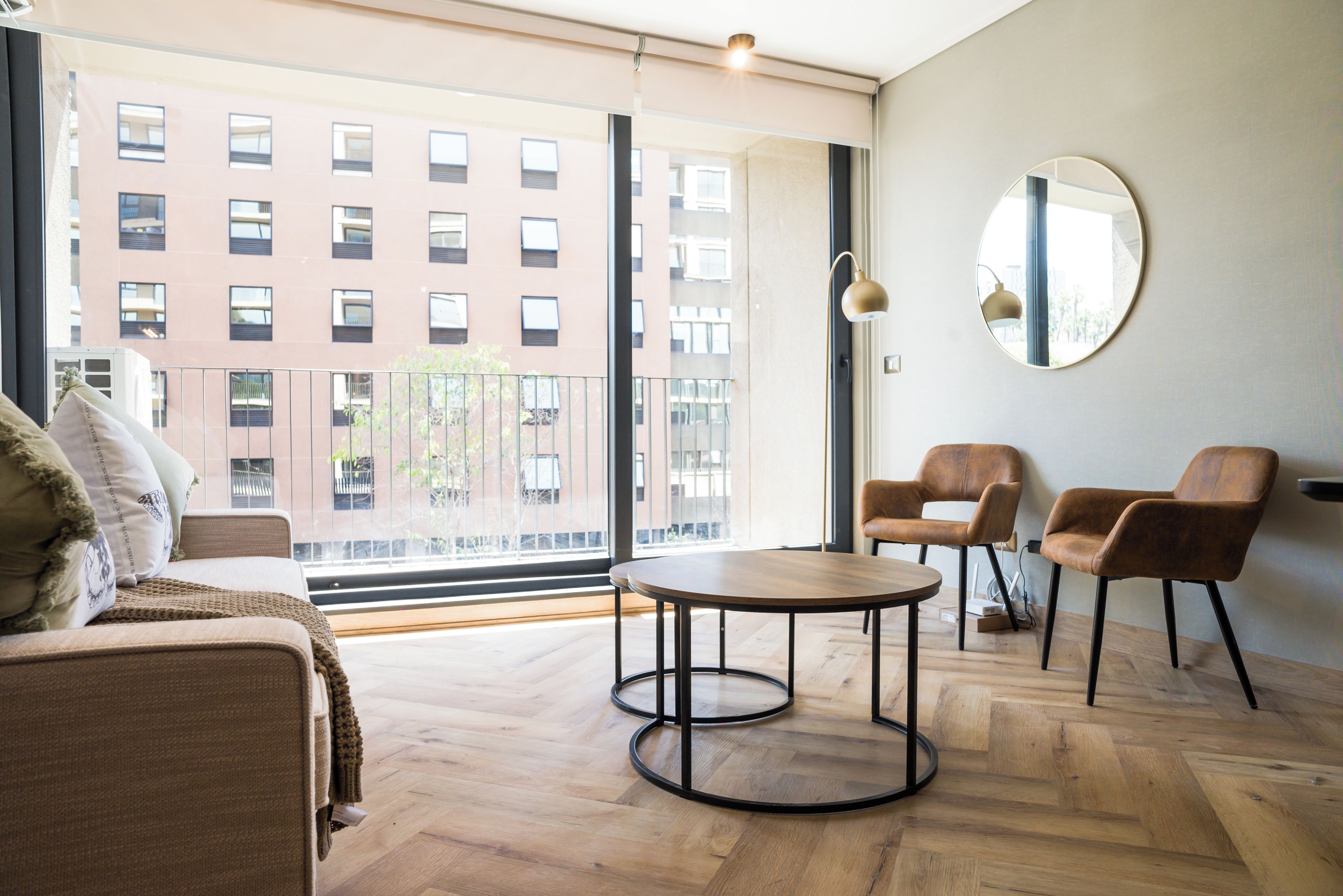 Ein modernes Wohnzimmer mit einer Couch, zwei Sesseln, einem runden Tisch und einem großen Fenster mit Blick auf ein Gebäude.