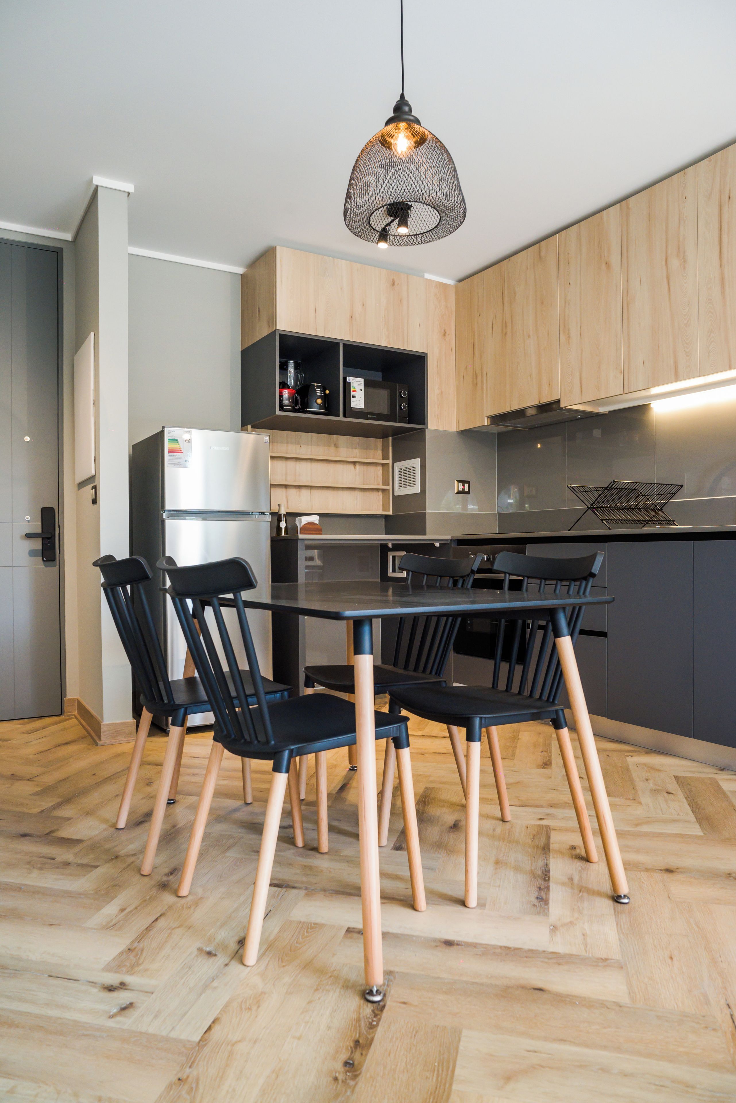 A modern kitchen with a dining area, featuring a black table, chairs, and a hanging light fixture.