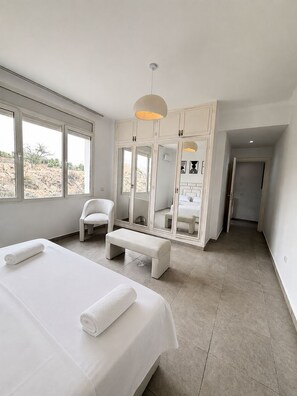 Quarto com uma cama grande, um banco, uma cadeira e um guarda-roupa espelhado.