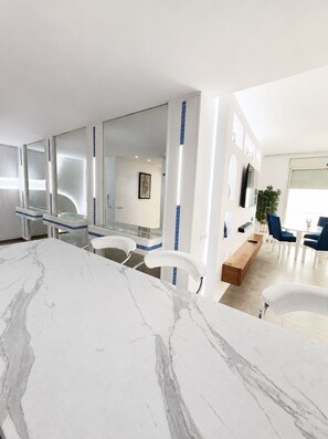 A modern interior with a marble countertop, white chairs, a wooden bench, and a large mirror. - Panoramic Atlantic Ocean view, first-row location | 2 minutes from the beach (Agadir)