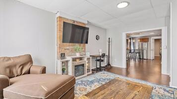 Ein Wohnzimmer mit einer Couch, einem Kamin, einem an einer Ziegelwand befestigten Fernseher und einem Essbereich mit Stühlen und einem Tisch.
