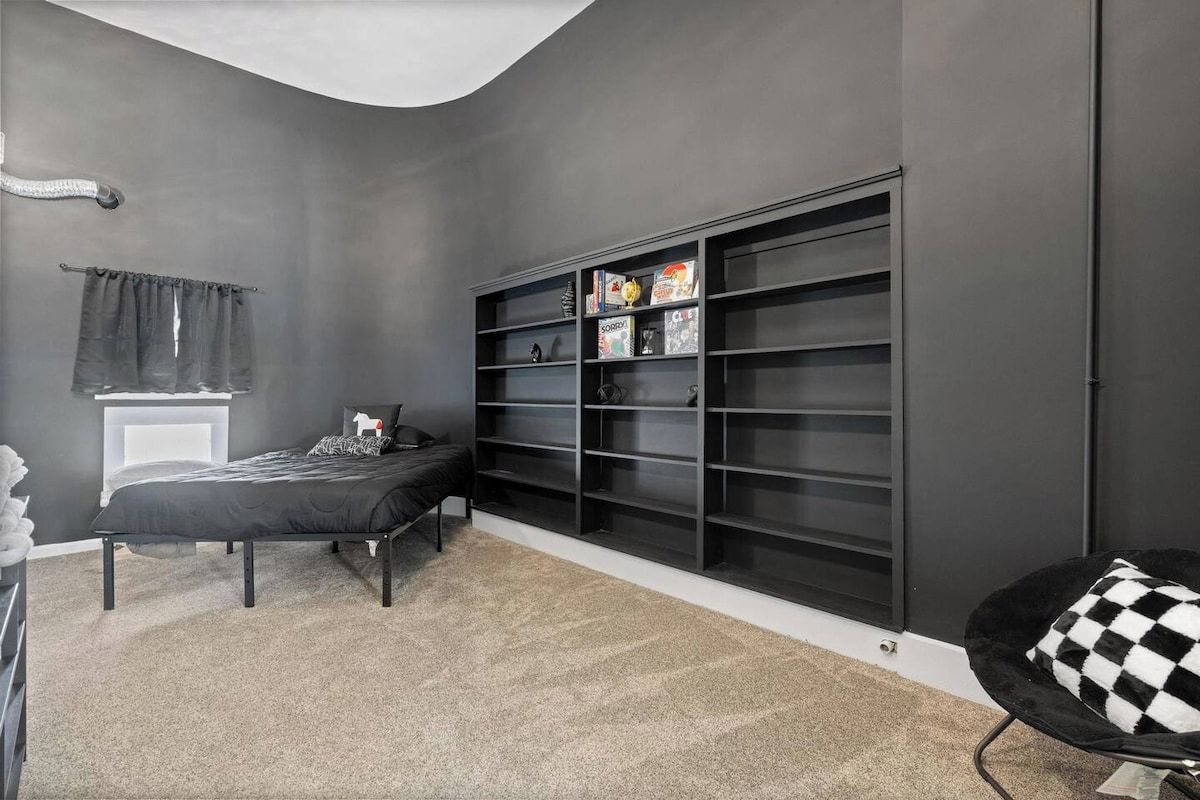 A bedroom with a bed, a large black shelving unit, and a checkered chair.
