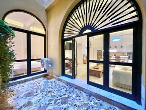 Un couloir d’hôtel avec des fenêtres en arc de cercle, un sol carrelé et une vue sur une cuisine moderne et un espace de vie.