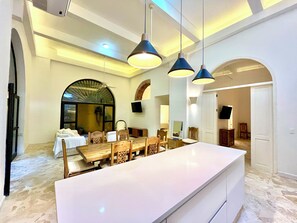Un grand espace dédié à la salle à manger, avec une longue table et des chaises, un comptoir blanc et un ventilateur de plafond.