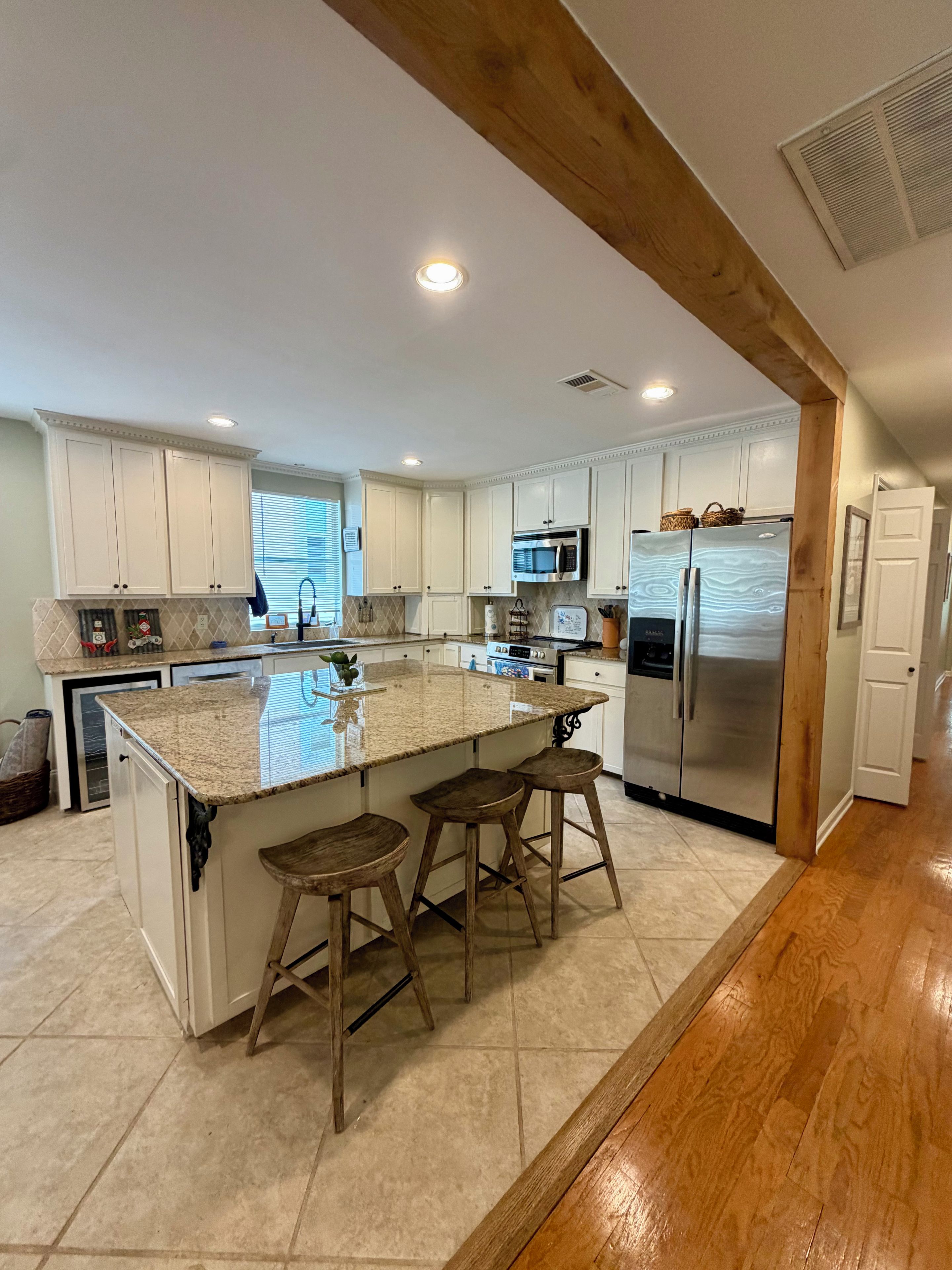 A modern kitchen with white cabinets, a stainless steel refrigerator, a microwave, and a granite island with bar stools.