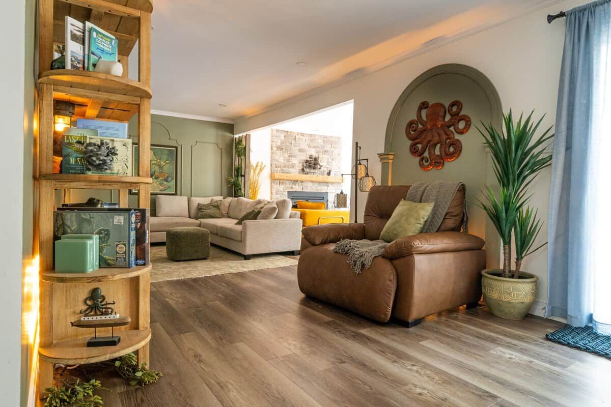 A living room with a brown leather sofa, a wooden bookshelf, and a potted plant.