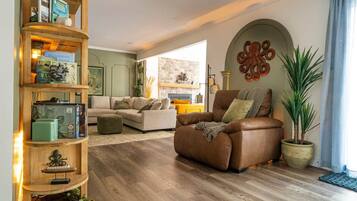 A living room with a brown leather sofa, a wooden bookshelf, and a potted plant.