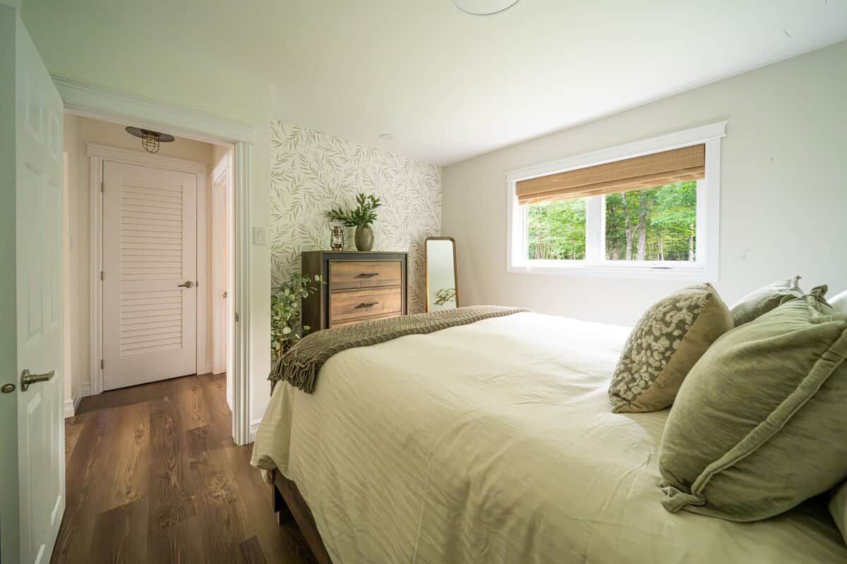 A bedroom with a bed, a dresser, a mirror, and a window with a view of trees.