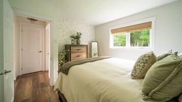 A bedroom with a bed, a dresser, a mirror, and a window with a view of trees.