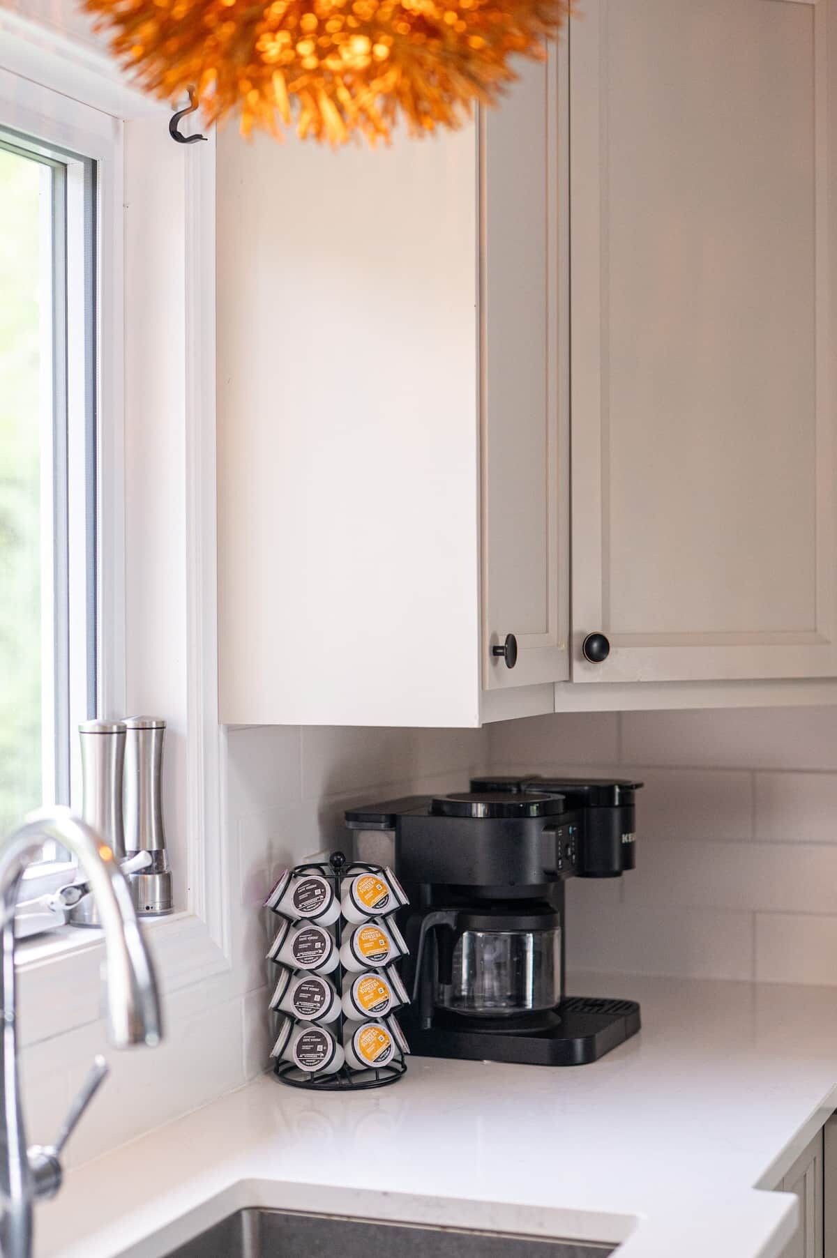 A kitchen with white cabinets, a coffee maker, and a coffee pod holder.