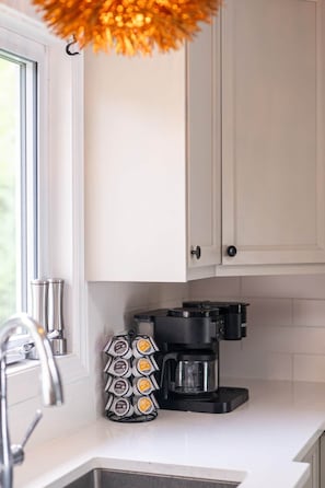 Una cocina con armarios blancos, una cafetera y un soporte para cápsulas de café.